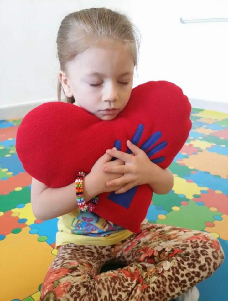 A girl with her eyes closed, holding a red heart cushion