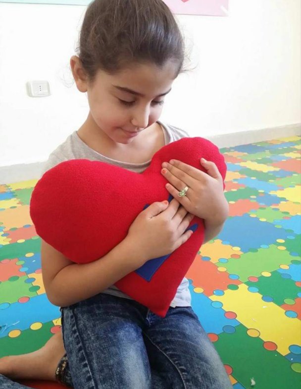 A girl holding a red heart cushion to her chest